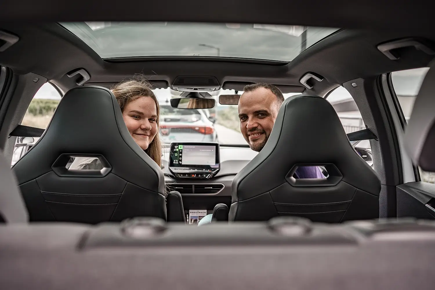 Fahrschülerin und Fahrlehrer am Steuer eines geparketen Autos drehen sich zu dem Insassen auf der Rückbank um