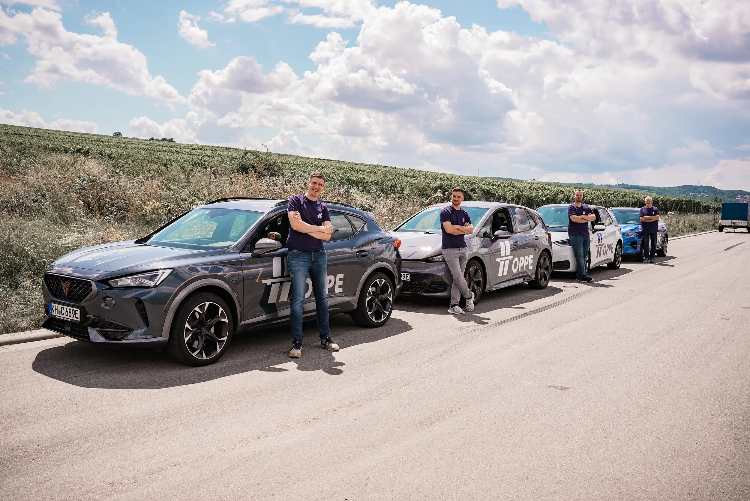 Die 4 Fahrerlehrer der Fahrschule Hoppe stehen vor ihren Fahrschulautos auf einer Straße in den Weinbergen in Bad Kreuznach