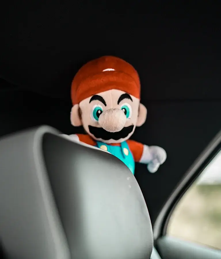 Super Mario Stoffpuppe schaut über die Rückenlehne eines Autositzes